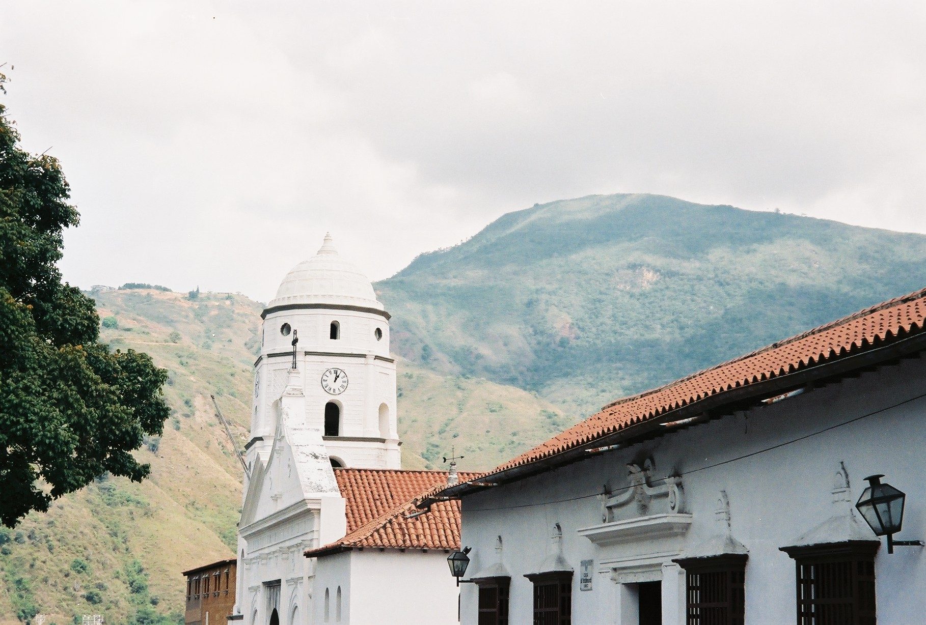 La catedral blanca de Trujillo y una casa colonial de techo de tejas, con la montaña verde detrás
